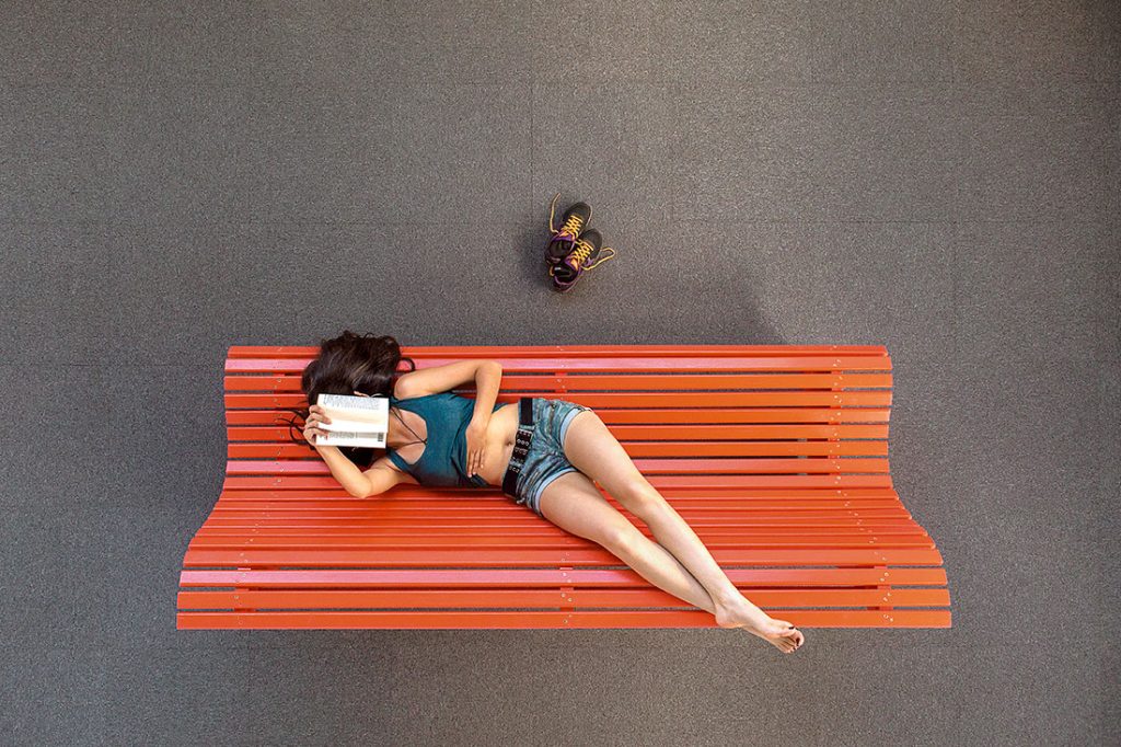 Une jeune fille allongée sur un banc rouge lit un livre